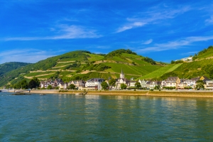 Flusslandschaft mit grünen Hügeln und kleinen Häusern am Ufer.