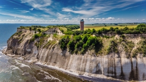 Klippenlandschaft mit Leuchtturm und bewölktem Himmel am Meer.