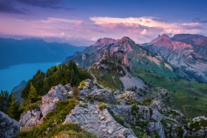 Berglandschaft mit felsigem Grat, grünem Tal und blauem See unter einem rosa Himmel.