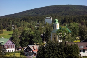 Dorf mit Kirche und grünen Wäldern im Hintergrund.
