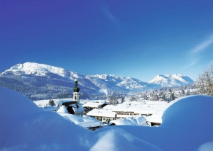 Winterlandschaft in Reit im Winkl mit verschneiten Bergen und Kirche im Vordergrund.