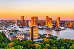 Skyline von Rotterdam bei Sonnenuntergang mit Erasmusbrücke und Hochhäusern am Wasser.