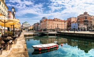 Kanal mit Boot, umgeben von historischen Gebäuden und Straßencafés unter blauem Himmel.