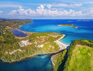 Luftaufnahme einer tropischen Küste mit klarem blauem Wasser und bewaldeten Inseln.