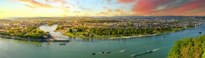 Panoramablick auf eine Flusslandschaft bei Sonnenuntergang mit Stadt und Schiffen.