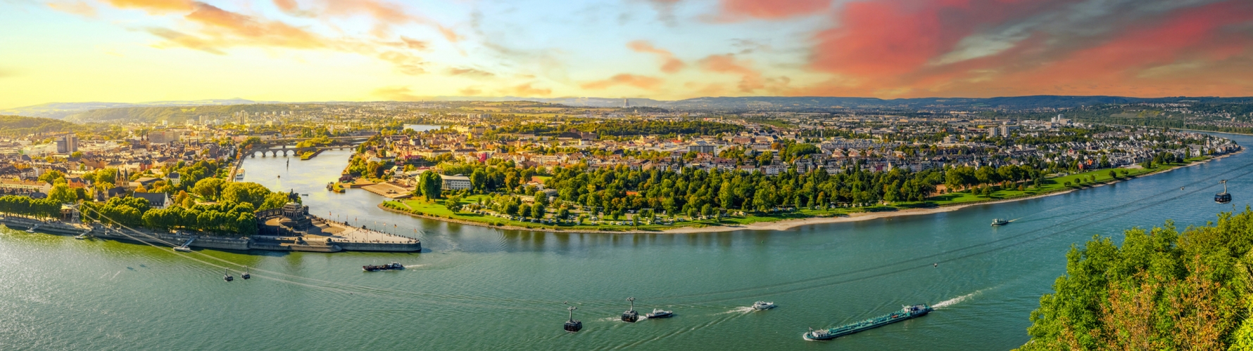 Panoramablick auf eine Flusslandschaft bei Sonnenuntergang mit Stadt und Schiffen.