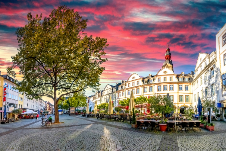 Historischer Marktplatz mit Tischen, Stühlen und farbenprächtigem Sonnenuntergangshimmel.
