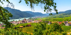 Panoramablick auf ein Dorf mit Fluss und umliegenden Bergen bei klarem Himmel.