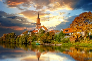 Kirchturm und Häuser am Fluss im Sonnenuntergang.