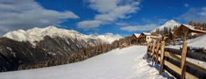Verschneite Alpenlandschaft mit Holzhäusern und blauen Himmel.