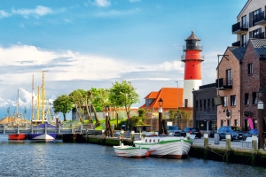 Küstenstadt mit Leuchtturm, Segelbooten und roten Backsteinhäusern am Wasser.