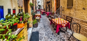 Enge Gasse mit Tischen und Stühlen vor einem Restaurant.