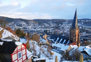Winterliche Stadtansicht mit verschneiten Dächern und Kirchturm im Vordergrund.
