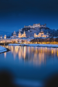 Verschneite Stadt und Festung, ruhig reflektiert in einem Fluss bei Abenddämmerung.