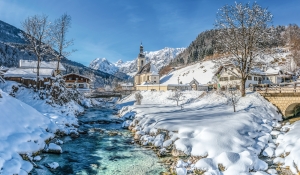 Verschneites Dorf mit Kirche und Bach im Winter.