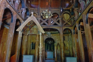 Innenraum einer Holzkirche mit dekorativem Holzschnitzwerk und Kronleuchter.