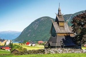 Holzkirche vor Bergen mit Häusern im Hintergrund.