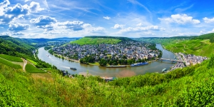 Panoramablick auf eine Flussbiegung mit Stadt und grünen Hügeln unter blauem Himmel.