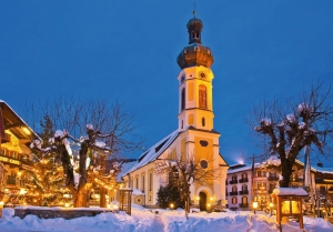 Beleuchtete Kirche und Gebäude im Schnee bei Dämmerung in einem Dorf.