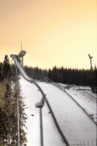 Eine verschneite Skisprungschanze umgeben von Bäumen bei Sonnenuntergang.