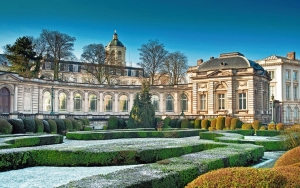 Historisches Gebäude mit gepflegtem Garten und gewölbten Fenstern vor blauem Himmel.