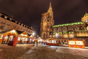 Weihnachtsmarkt bei Nacht vor beleuchteter Kathedrale.