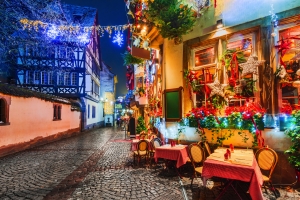 Beleuchtete, festliche Gasse mit Café und Fachwerkhäusern bei Nacht.