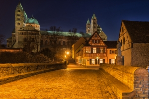 Pflasterstraße in der Nacht vor einer beleuchteten Kathedrale und Fachwerkhäusern.