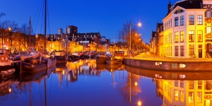 Boote und Gebäude entlang eines Kanals bei Abenddämmerung mit Lichtern reflektiert im Wasser