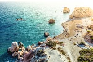 Küste mit Felsen und klarem Meerwasser, Menschen genießen den Strand.