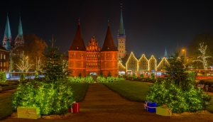 Weihnachtsmarkt vor beleuchtetem Holstentor in Lübeck bei Nacht