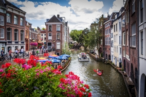 Blick auf einen belebten Kanal in einer Stadt mit Booten und blühenden Pflanzen.