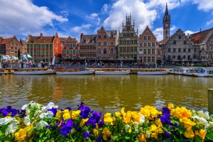 Blumenbeet vor bunten Häusern und Kanal in einer historischen Stadt bei klarem Himmel.