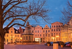 Historischer Marktplatz mit Brunnen und beleuchteten Gebäuden bei Abenddämmerung.