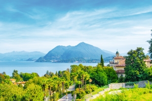 Landschaft am See mit Bergen im Hintergrund und einem Gebäude im Vordergrund.