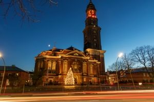 Beleuchtete Kirche bei Dämmerung mit Weihnachtsbaum im Vordergrund.