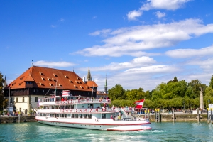 Weißes Ausflugsschiff vor historischem Gebäude an einem Flussufer bei sonnigem Wetter.