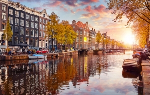 Kanal in Amsterdam bei Sonnenuntergang, mit Booten und herbstlichen Bäumen.