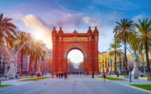 Triumphbogen in Barcelona bei Sonnenschein mit Menschen und Palmen umgeben.