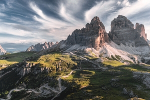 Berglandschaft mit dramatischem Himmel und kurviger Straße im Vordergrund.