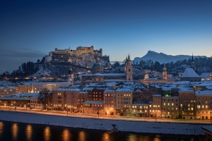 Verschneite Stadt und Burg bei Abenddämmerung, beleuchtet entlang eines Flusses.