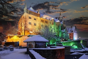 Beleuchtetes Schloss im Winter bei Sonnenuntergang, umgeben von Schnee und Bäumen.