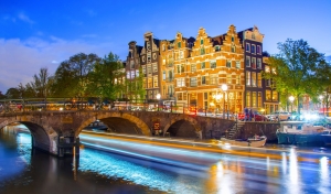 Kanal mit beleuchteter Brücke und historischen Gebäuden bei Abenddämmerung.