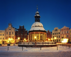 Winterliche Wasserkunst und historische Gebäude bei Nacht, verschneit.