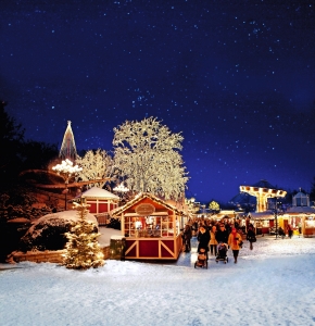 Weihnachtsmarkt bei Nacht mit festlichen Lichtern und Besuchern im Schnee.
