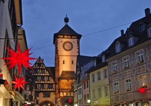 Historischer Uhrturm und Fachwerkhäuser bei Abenddämmerung, dekoriert mit Weihnachtssternen.