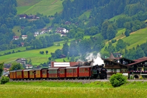 Dampflok fährt durch malerische Alpenlandschaft mit grünen Hügeln im Hintergrund