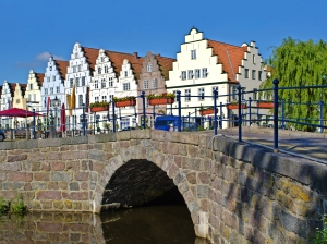 Historischer Gebäudekomplex mit Giebeln hinter Steinbrücke und Wasser.