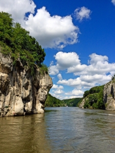 Fluss zwischen hohen Felsklippen mit blauem Himmel und Wolken.