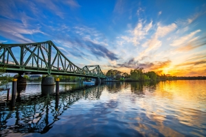 Eine Brücke über einem Fluss bei Sonnenuntergang mit buntem Himmel und spiegelnden Wasseroberflächen.